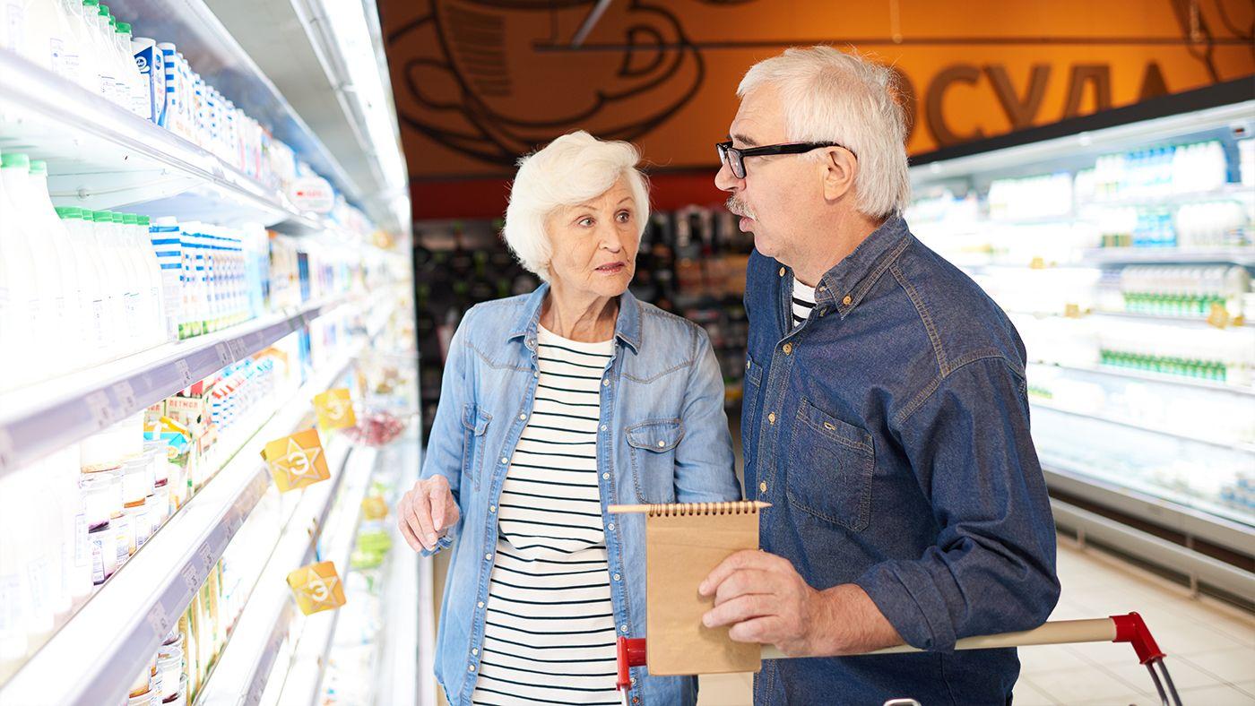 Elderly couple shopping in a grocery store, discussing medication options for cough relief, highlighting the importance of prescribed cough medications. 