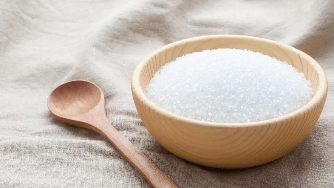 Wooden bowl filled with sugar with a wooden spoon beside it, symbolizing the management of blood sugar levels for diabetes care.