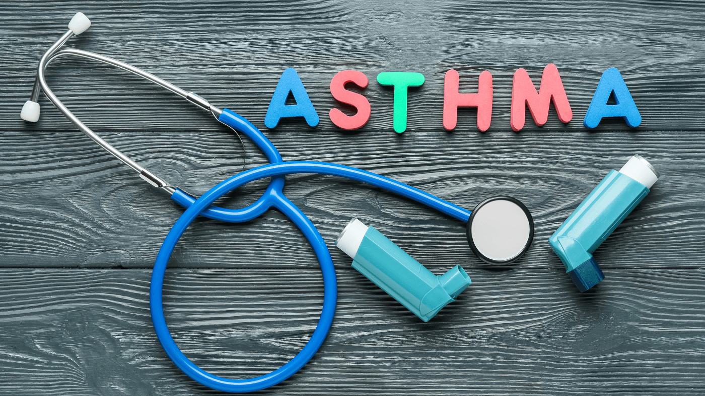 Estetoscopio e inhaladores para el asma sobre una superficie de madera con la palabra "Asma" escrita en letras coloridas.
