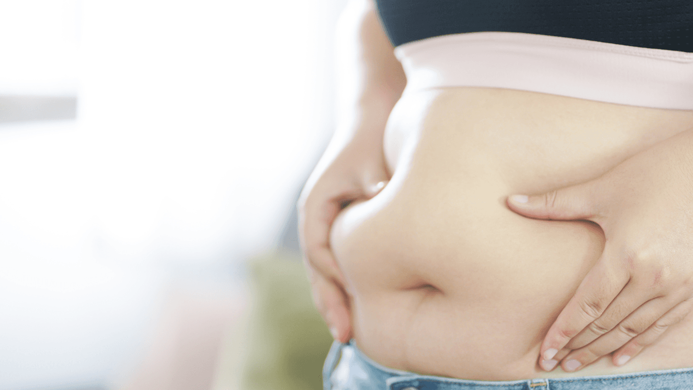 Un primer plano de una persona pellizcando su cintura, representando los desafíos de la obesidad y la importancia del manejo del peso.